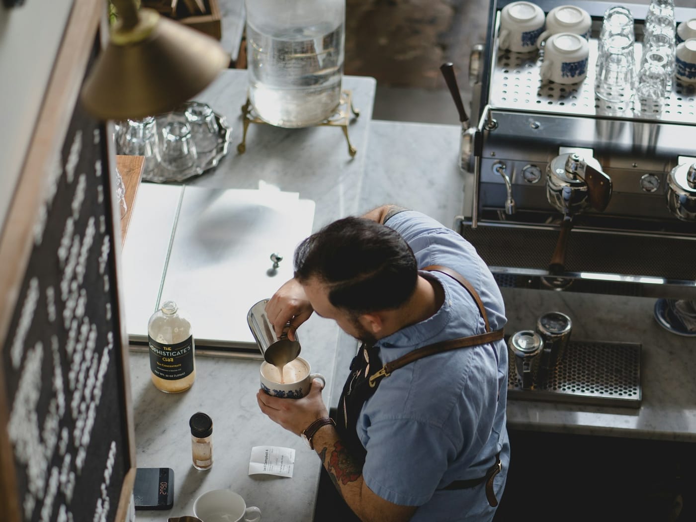 How to Calculate Hours Worked — Barista working at a coffee shop counter where staff clock in on a tablet kiosk